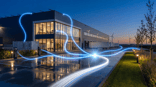 Modern commercieel vastgoed in de schemering met blauwe lichtstromen die energie symboliseren, windmolens op de achtergrond — visualisatie van geëlektrificeerd vastgoed door Sampre.